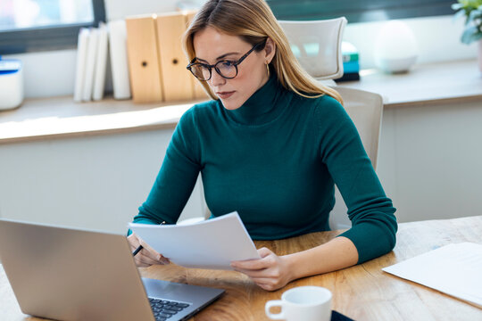 Focused blond businesswoman preparing documents on laptop in office