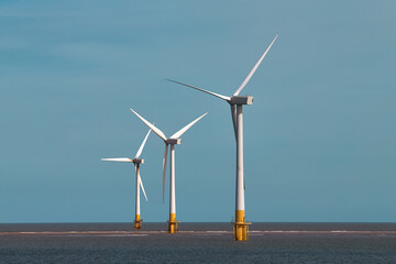 Three offshore wind turbines standing in the sea, with clear blue sky. Wind Turbines at Sea....