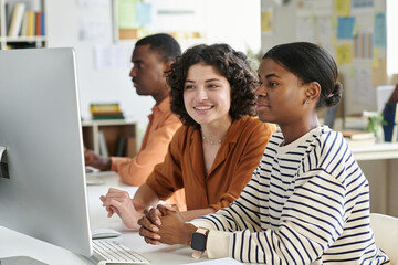 Multiracial team engaging in collaborative work at computer stations in modern office space, with...