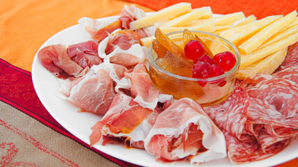 Meat and cheese platter on a white plate. Fruit mostarda, candied pear in syrup, candied red cherries in syrup, mustard sauce, traditional Italian mostarda sauce, sauce for cheese, for meat.