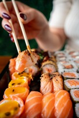 Hand picking sushi with chopsticks from a platter.