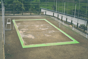An aerial view of a volleyball court with a green border and white lines, surrounded by a fence and trees.