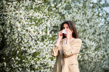 Woman allergic suffering from seasonal allergy at spring in blossoming garden at springtime. Young...