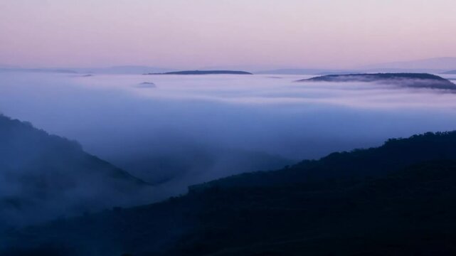 Wide shot of Twilight fog rolling over hills at dusk, with the camera slowly zooming in to emphasize the misty effect.