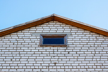 The roof of a charming white brick building features a small window present