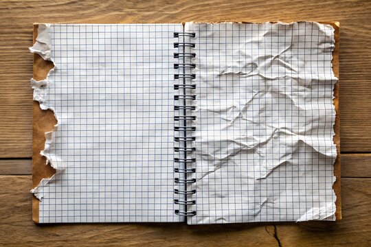 Open notebook with torn and crumpled grid pages on a wooden surface, showcasing a vintage, rustic aesthetic for journaling or note-taking themes.