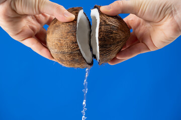 Hands open coconut, coconut water pour out, blue background