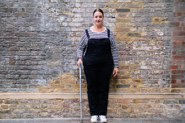 Mature woman with disability holding walking cane in front of brick wall