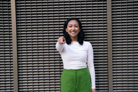 Smiling woman pointing and standing near wall