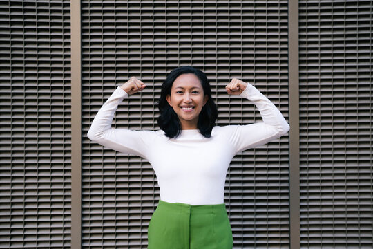 Smiling woman flexing muscles and standing in front of wall