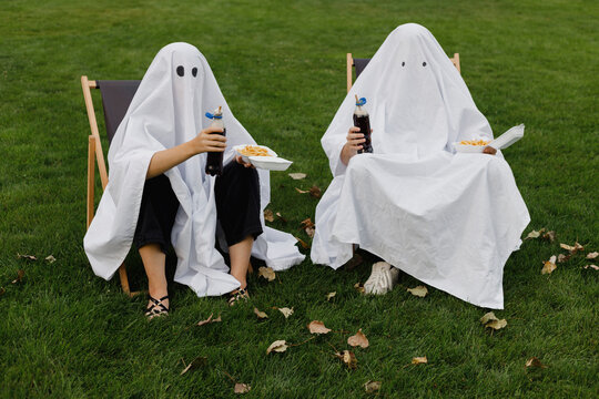 Couple wearing ghost costumes sitting with fries and cold drinks on chair