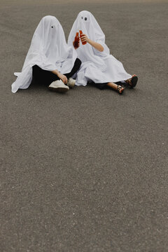 Couple wearing ghost costumes and toasting beer bottles on road