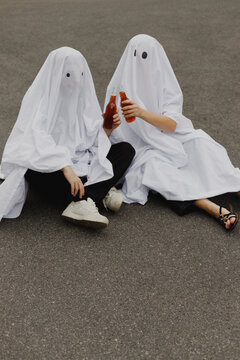 Young couple wearing ghost costumes and toasting beer bottles on road