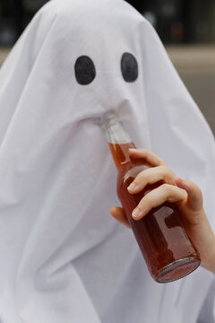 Young woman wearing ghost costume and drinking beer from glass bottle