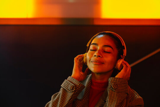 Woman enjoying music with eyes closed on headphones at illuminated subway station