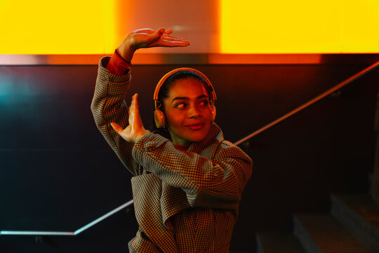 Woman listening music on headphones and dancing at subway station staircase