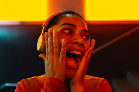 Woman with mouth open and head in hands wearing headphones at night