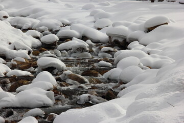 Frozen water and snow covered stone of a mountain river in winter