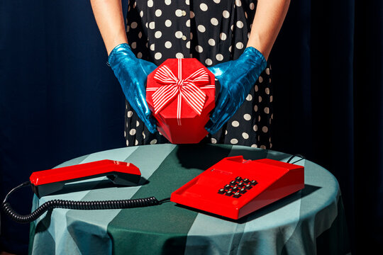 Woman in polka dots dress holding red gift box over table in studio