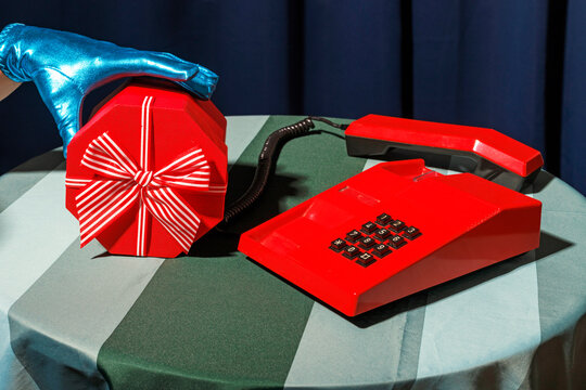 Hand of woman wearing futuristic glove picking up Christmas present by retro telephone on table