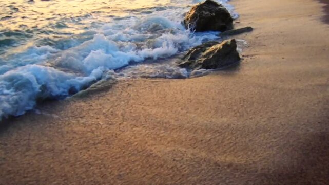 Waves gently lap at shore during stunning sunset over ocean. Golden sunlight reflects off waves as they roll onto shore, creating tranquil atmosphere at sunset by sea. Montenegro summer, Canj