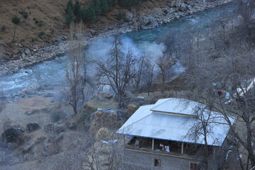 Smoke originating from a lone hut, located with a river in mountains