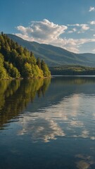 Fototapeta premium Mountain lake surrounded by lush green forests, with reflection of trees and sky visible in calm waters