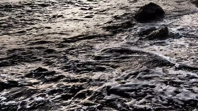 Waves gently lap at shore during stunning sunset over ocean. Golden sunlight reflects off waves as they roll onto shore, creating tranquil atmosphere at sunset by sea. Montenegro summer, Canj