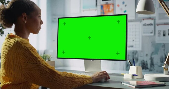 Black Female Engineer Engages With Desktop Computer Featuring Green Chroma Key Screen. Modern Office Engineering and Creative Tasks, Technology and Innovation. Zoom Out Shot
