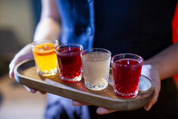 Bartender serving a flight of colorful juices and fruit extracts on a wooden tray, offering a refreshing and healthy beverage option