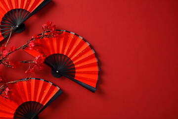 Traditional Asian paper fans with red blossoms on a vibrant red background. Chinese New Year, Lunar New Year 2025 concept.