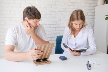 Fototapeta premium young male patient testing hearing aid in clinic exam room, female doctor helping