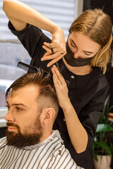 Female hairdresser cutting hipster male male haircut in hairdressing salon. Barber does the correct trimming with a comb long length of hair. Male hair cut, close-up. Hairdresser cutting, man's hair