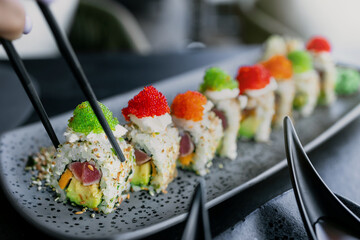 Colorful sushi rolls served on a stylish gray platter with chopsticks