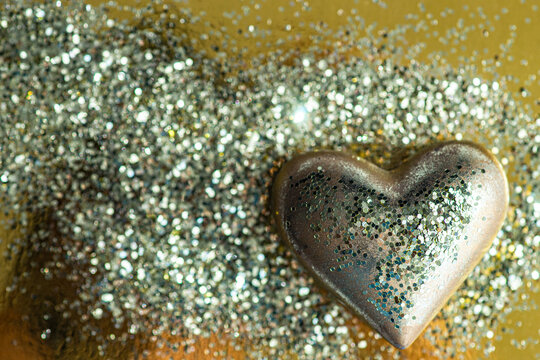 Close-up of a gold heart ornament covered with silver glitter on a golden background