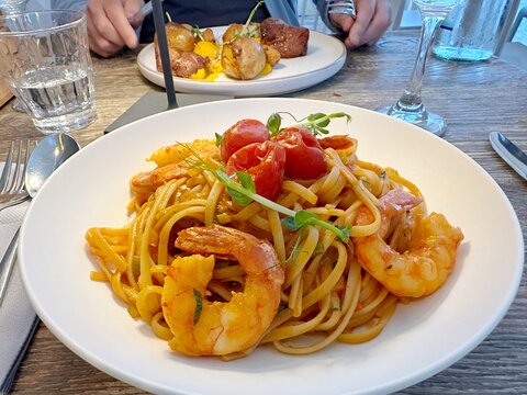 Plate of linguine with prawns, lobster bisque and tomatoes and a man eating meat and potatoes