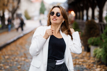 Fototapeta premium Stylish Young Woman in Sunglasses Walking Through a Leafy Street in Autumn