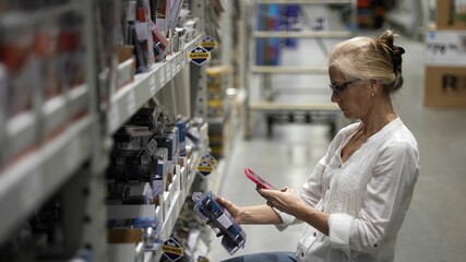 Mature woman using smart phone to take photo of door knobs for sale in a big box hardware store...