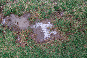 Patches of soil with a reddish hue interspersed with sparse grass, the soil appears to have a slightly damp texture and lighter patches, natural abstract background 