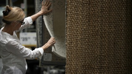 Happy mature woman hand touching carpet sample while looking through rugs for home remodeling redecorating project, in a home decorating store.