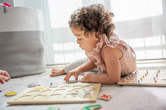 Close-up image of a little girl lying on a play mat playing with a wooden alphabet letter puzzle. Montessori methodology and materials. education, development and learning in the childhood stage.