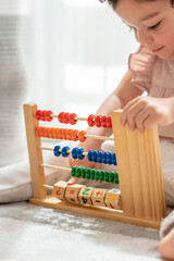 little girl playing sitting on the carpet in her room with a wooden toy made of beads, numbers and colors. montessori material concept development and learning in the childhood stage.