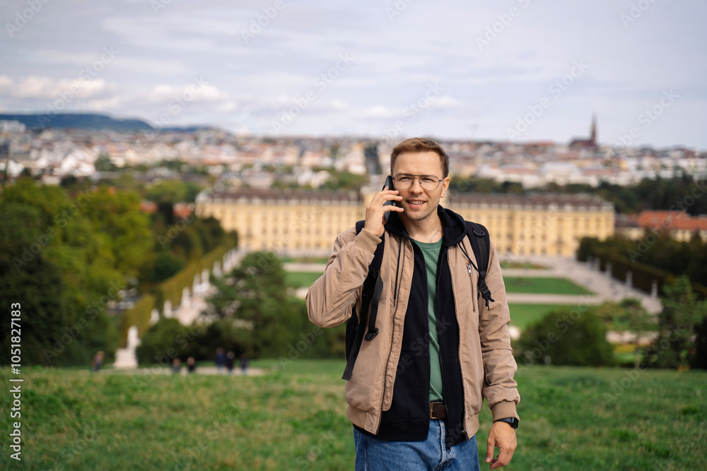 Wall mural young man backpacker talking on phone while walking in the city. handsome male tourist traveler trav