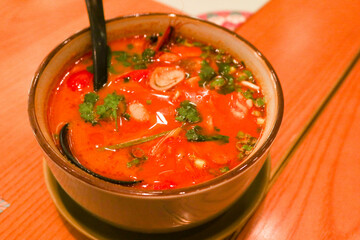 close up of Thai sour dish Tom Yum ( Tom Yan) soup with seafood, mushroom and coriander in a bowl with a big black spoon 