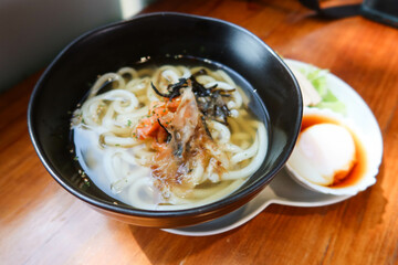 close up of Japanese soup udon noodles with salmon and seaweed. A half boiled egg (onsen egg) and veggie salad on the side