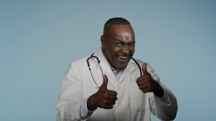 Happy joyful african american man doctor showing thumb up in studio blue background male customer healthcare worker show OK agreement approval sign recommendation promotion satisfied medical service