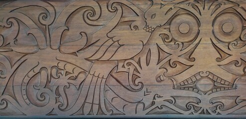 Carvings on a wooden wall featuring traditional Dayak motifs, including the hornbill bird, a dragon-like creature, and a broad face with large eyes.