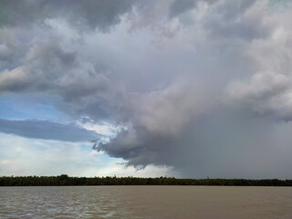 A view of thick clouds pouring heavy rain over the land and river below, creating a misty atmosphere.
