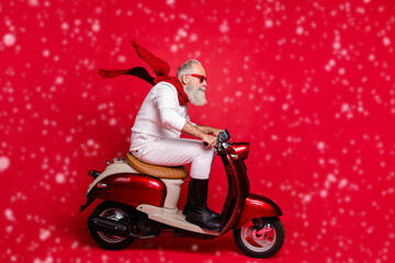 Cool aged santa man rushing newyear party by bike wear sun specs jumper and trousers isolated red...