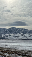 Fototapeta premium The sun breaks through the clouds over snow-covered mountains in Kyrgyzstan. A beautiful sight for winter tourism and mountain adventures.